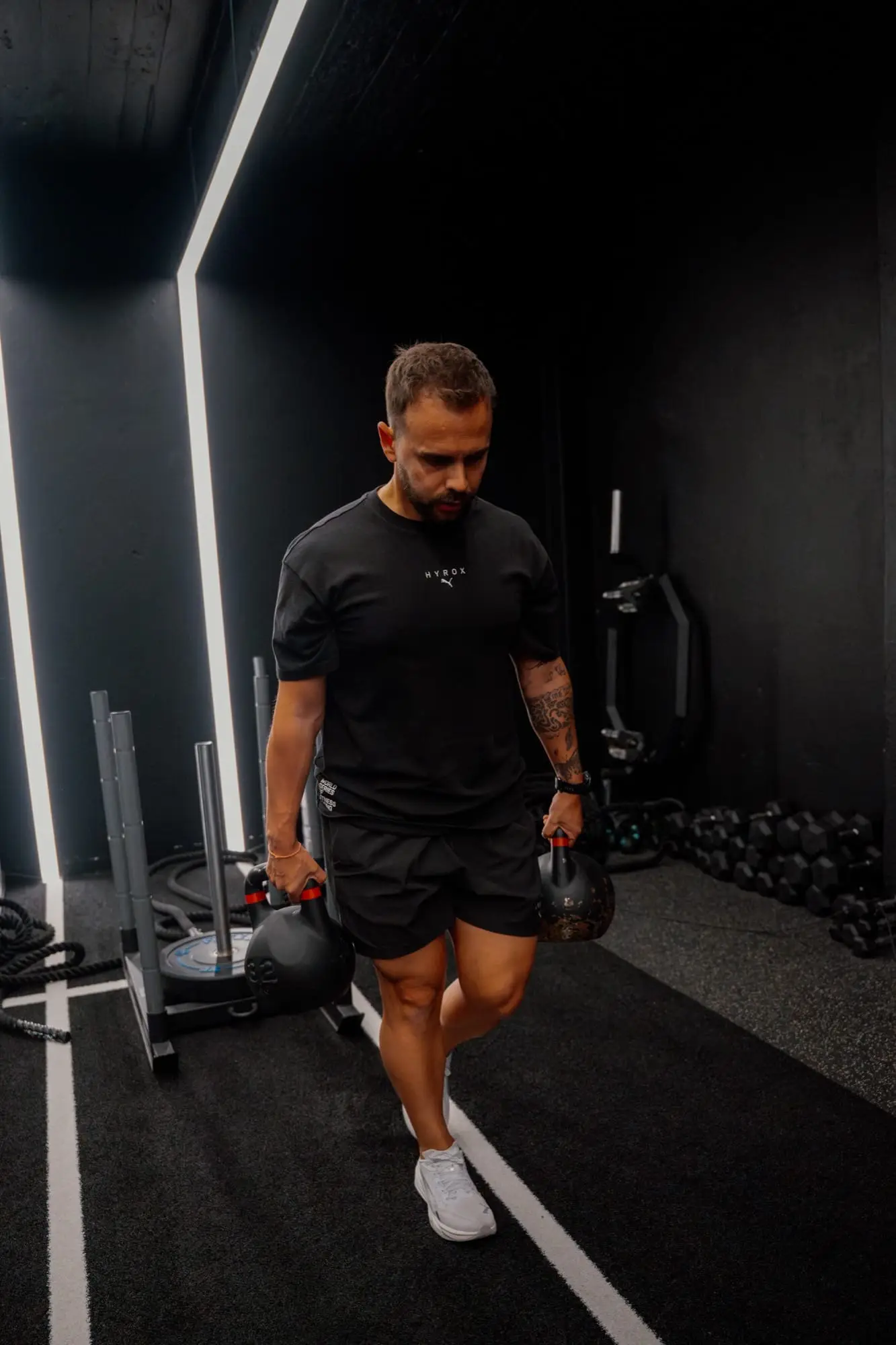 Treinador da AF Program em treino de força para HYROX, com kettlebells num ginásio.